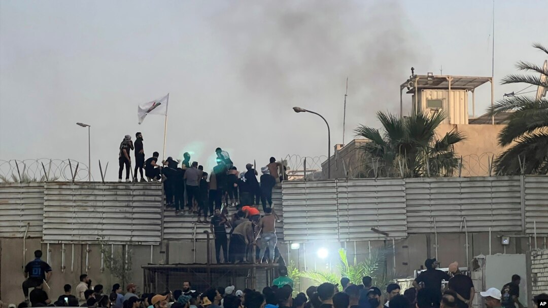 Protesters scale a wall at the Swedish Embassy in Baghdad Thursday, July 20, 2023. Protesters angered by the planned burning of a copy of the Quran stormed the embassy early Thursday, breaking into the compound and lighting a small fire.
