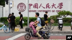 北京街头人们路过中国人民大学校园外墙的标识。（2024年7月22日）