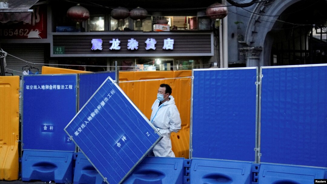 上海一名身穿防護服的工作人員站在封城使用的圍欄旁。 （2022年4月11日）