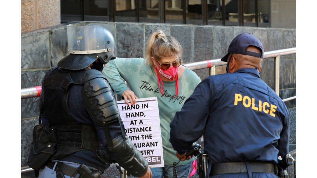 FILE - Police warn a demonstrator working in the hospitality industry during a protest against lockdown regulations in the streets close to Parliament in Cape Town, South Africa, July 24, 2020.