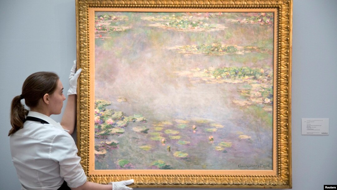 A gallery assistant poses with the painting Nympheas by Claude Monet at a photo-call for Impressionist and Modern Art Evening Sale at Sotheby's auction house in London, June 18, 2014.