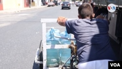 Carretillas cargadas con botellones que van y vienen de un pozo de agua público. [Foto: Nicole Kolster/VOA]