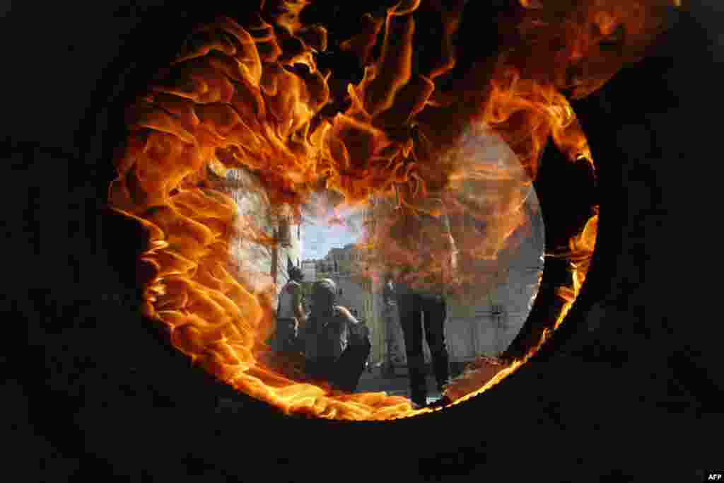 Palestinian protesters are seen through a burning tyre during clashes with the Israeli soldiers after the Friday prayers in the centre of the occupied West Bank city of Hebron.
