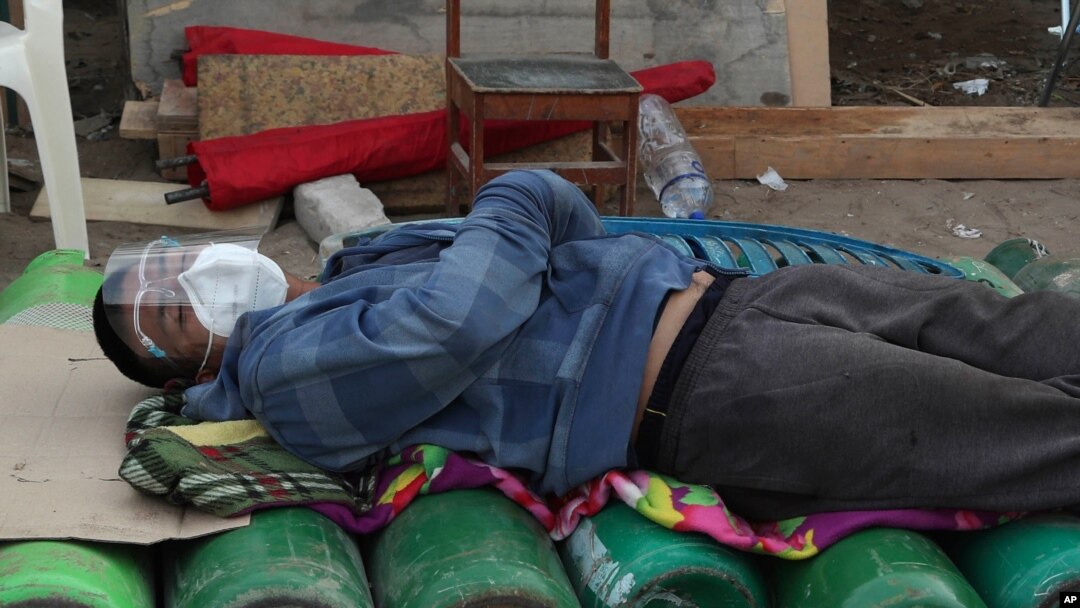 A man sleeps on top of empty oxygen cylinders, waiting for a shop to open to refill his tank, in Lima early Feb. 18, 2021, as the lack of medical oxygen to treat COVID-19 patients continues to be the norm in Peru.