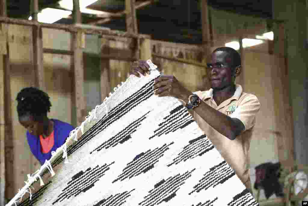 Manager of TEXFAD, John Baptist Okello checks a handmade carpet woven from banana fiber threads, at a factory in Sonde, Mukono District, Uganda, Sept. 20 2023. 