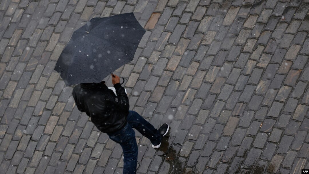 FILE - A man shelters under an umbrella as snow turns to sleet and rain in Berlin, Germany, May 7, 2021. 