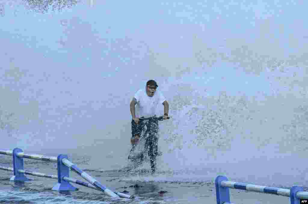 A man rides a bicycle as waves, caused by Typhoon In-Fa further down the Chinese coast, surge over a barrier along the seacoast in Qingdao in China's eastern Shandong province, July 25, 2021.