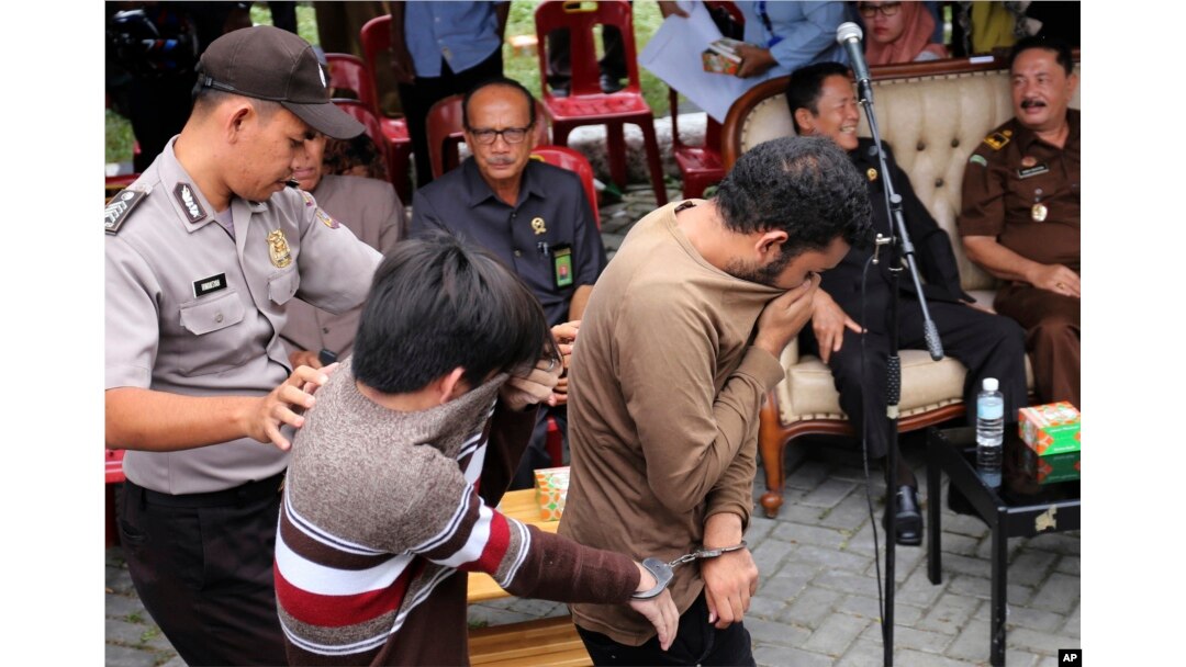 FILE - A police officer escort two men convicted of gay sex to be publicly caned at a mosque in Banda Aceh, Aceh province Indonesia, May 23, 2017.