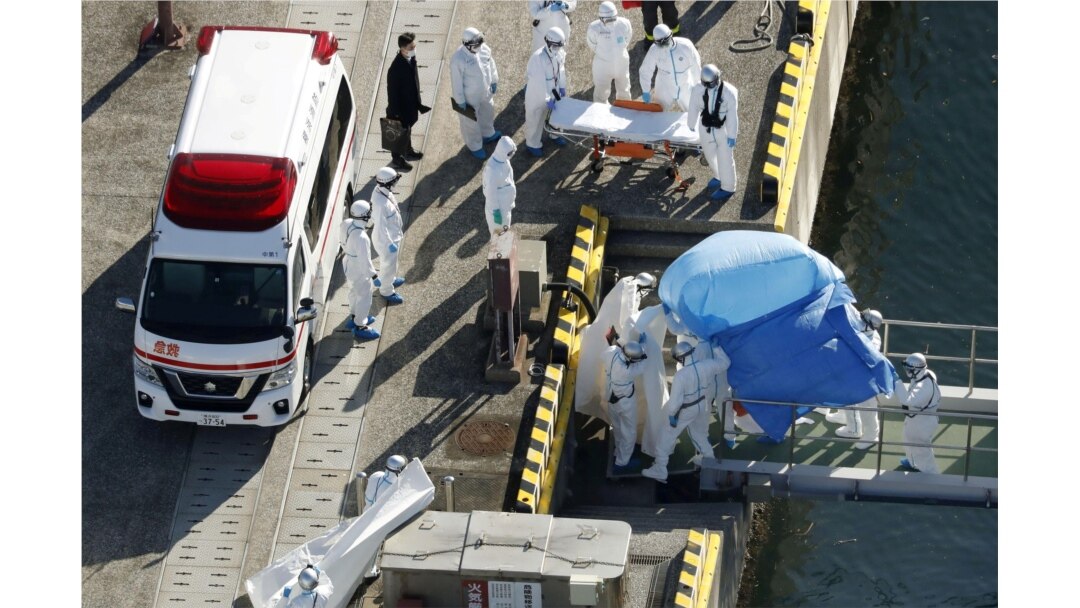 Officers in protective gear escort a person (under the blue sheet) who was aboard cruise ship Diamond Princess and tested positive for coronavirus, after the person is transferred to a maritime police base in Yokohama, Japan, Feb. 4, 2020.