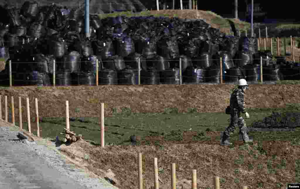 A man walks near waste containing radiated soil, leaves and debris from the decontamination operation at a storage site at Miyakoji area in Tamura, Fukushima prefecture, April 1, 2014.
