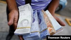 El asistente de un conductor de autobús sostiene billetes de Bolívar, por valor de entre 0,01 y 0,25 dólares estadounidenses, luego de que el Banco Central de Venezuela anunciara que recortará seis ceros de precios, en Caracas.