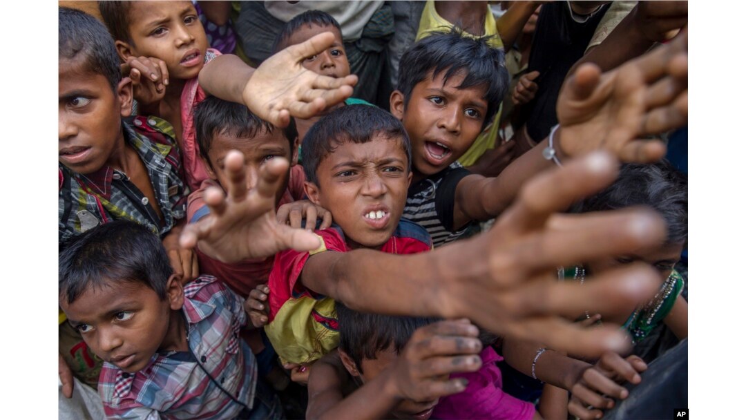 FILE - Rohingya Muslim children, who crossed over from Myanmar into Bangladesh, stretch out their arms out to collect chocolates and milk distributed by Bangladeshi men at Taiy Khali refugee camp, Bangladesh, Sept. 21, 2017.
