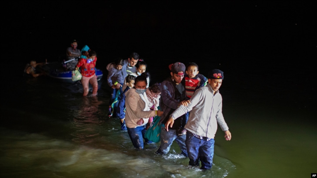 FILE - Migrant families, mostly from Central American countries, wade through shallow waters after being delivered by smugglers on small inflatable rafts on U.S. soil in Roma, Texas, March 24, 2021.