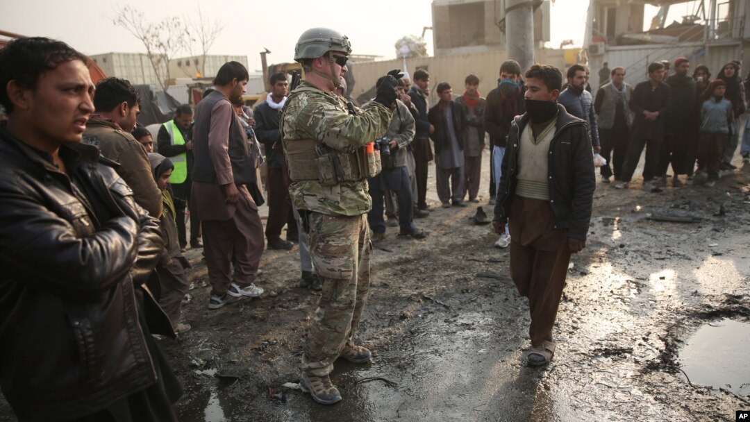 A U.S. soldier, center, takes a photo at the site of a suicide car bomb attack near the headquarters of the European Union police training mission in Kabul, Afghanistan, Jan. 5, 2015. 