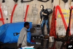 FILE - A migrant walks past a painting by English graffiti artist Banksy, at the entrance of the Calais refugee camp in France, in Calais, northern France, Monday, Dec. 21, 2015.