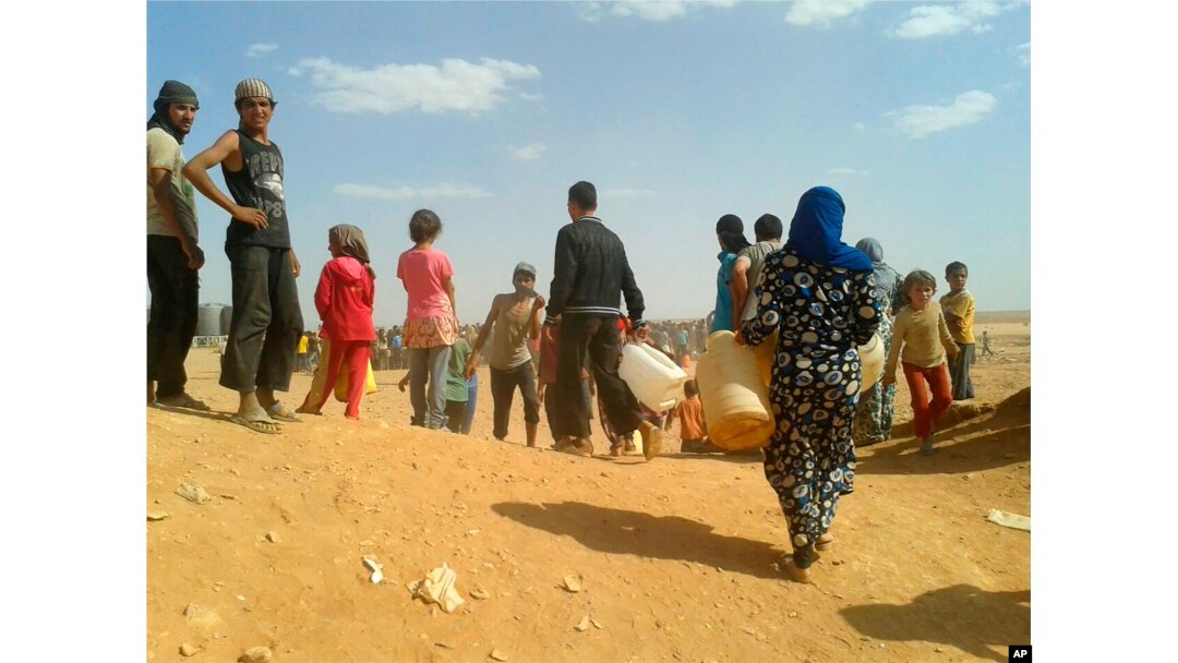 FILE - Syrian refugees gather for water at the Rukban camp for displaced Syrians, on the Jordan and Syria borders, June 23, 2016.