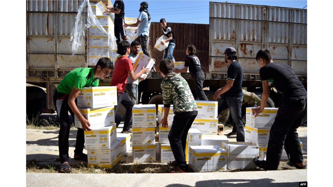 Syrian men carry aid parcels provided by the UN World Food Programm (WFP) and the Syrian Arab Red Crescent in the rebel-held town of Al-Houla, on the northern outskirts of Homs in central Syria, on May 25, 2016.