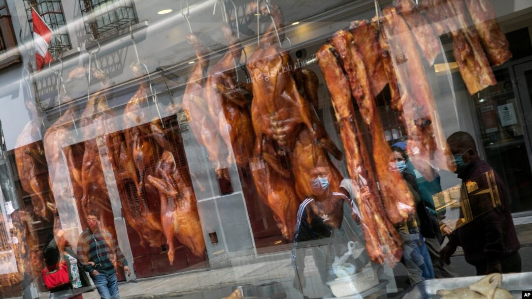 Pedestrians are reflected in the storefront window of a Chinese restaurant displaying roasted duck in downtown Lima, Peru, July 11, 2020, amid the new coronavirus pandemic.