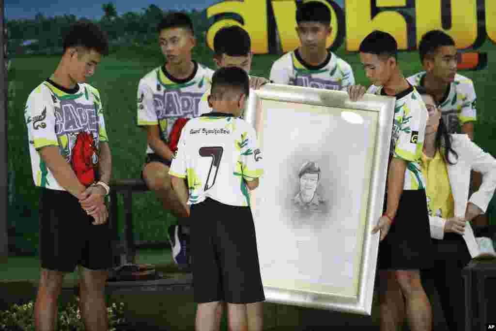 Coach Ekkapol Janthawong, left, and the 12 boys pay their respect and thanks as they hold a portrait of Saman Gunan, the retired Thai SEAL diver who died during their rescue attempt, during a press conference in Chiang Rai, northern Thailand.