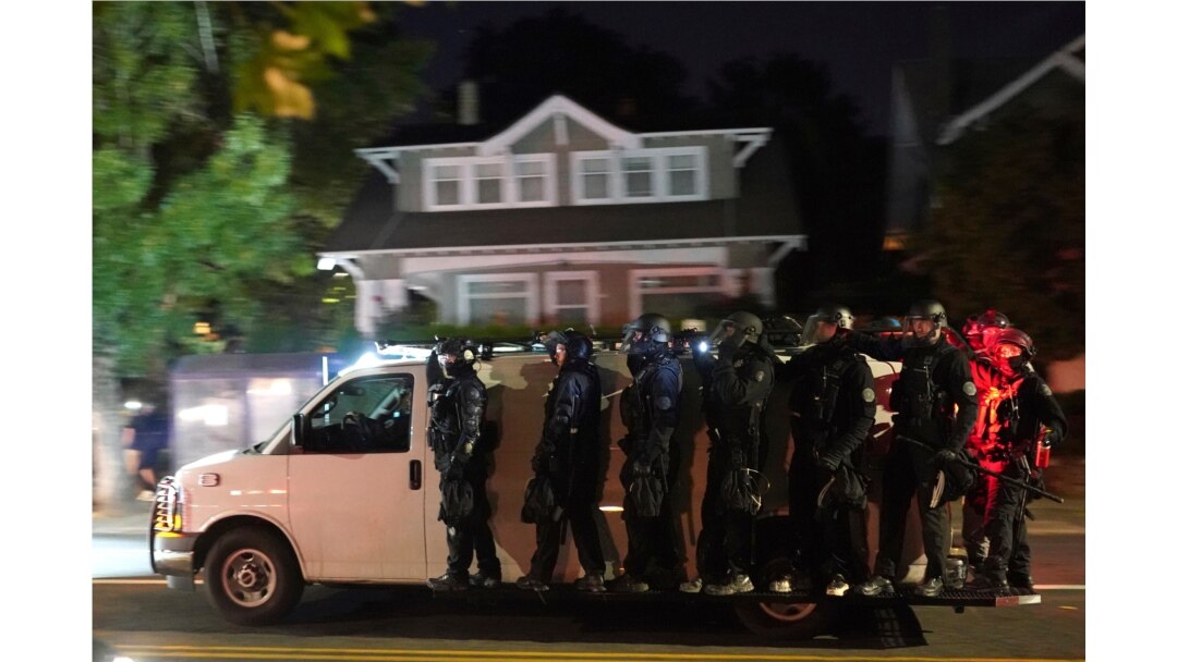 Portland police hang off the side of a riot van while searching for protesters in the Laurelhurst neighborhood after dispersing a crowd of about 200 people from in front of the Multnomah County Sheriff's Office on Aug. 8, 2020, in Portland, Ore.
