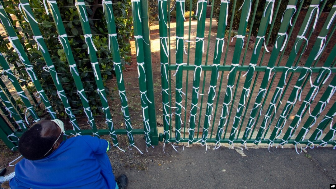 FILE - Silva Cossa, the caretaker, looks up as he ties ribbons onto a fence to represent a South African who has died from COVID-19, at St James Presbyterian Church in Bedford Gardens, Johannesburg, South Africa, July 29, 2020. 