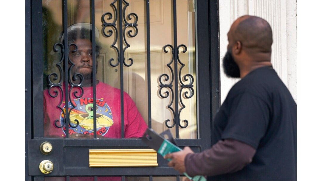 FILE - Anthony Brinson, right, talks with a resident while leaving a flyer at a home in Detroit, May 4, 2021. Officials are walking door-to-door to encourage residents of the majority Black city to get vaccinated against COVID-19.