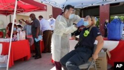 Hialeah Fire Department Firefighter-Paramedic Laura Nemoga, right, winces as medical assistant Jesus Vera performs a COVID-19 test, Aug. 6, 2020, at Hialeah Fire Station #1, in Hialeah, Florida.