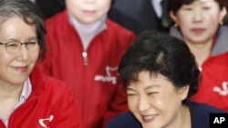 Park Geun-hye (R), interim leader of the ruling Saenuri Party, and party members smile as they watch a television report on an exit poll of the parliament elections at the party's headquarters in Seoul, April 11, 2012.