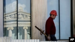 FILE - A worker carries construction material atop the 19th century Athens Academy building in central Athens, Greece.