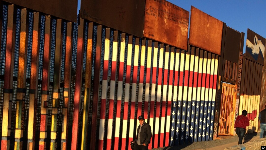 People pass graffiti along the border structure in Tijuana, Mexico, Jan. 25, 2017.