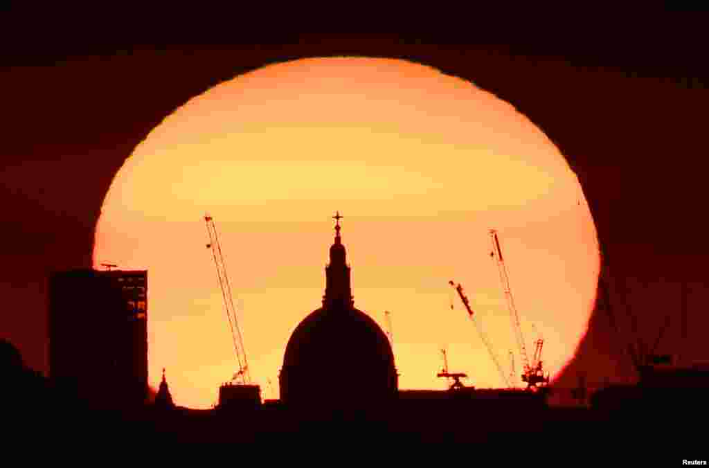 The dome of St. Paul&#39;s Cathedral and construction cranes are silhouetted by the rising sun at dawn in London.