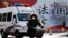 A woman and a police van pass a Chinese government propaganda billboard that reads "China Rule By Law" on a street in Beijing, Dec. 28, 2016. Many in China are infuriated by a decision to drop charges in a high-profile police brutality case.