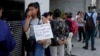 资料照片: 2024年2月5日一名妇女在阿根廷人力资本部长办公室外与其他人一起排队等待援助。标语牌上面西班牙语写着：“我是贝蒂，一名学生，我没有足够的食物”。 