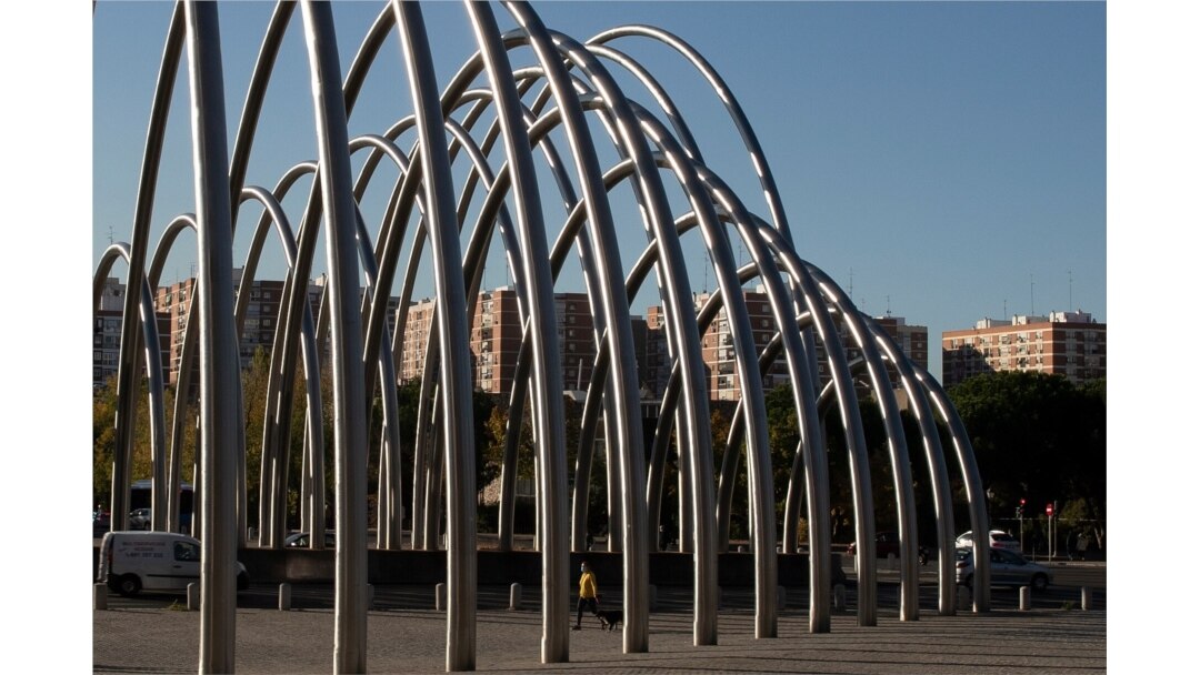 A woman wearing a face mask to protect against the spread of coronavirus walks beneath the metal Puerta de la Ilustracion urban sculpture designed by Andreu Alfaro in Madrid, Spain, Oct. 15, 2020.