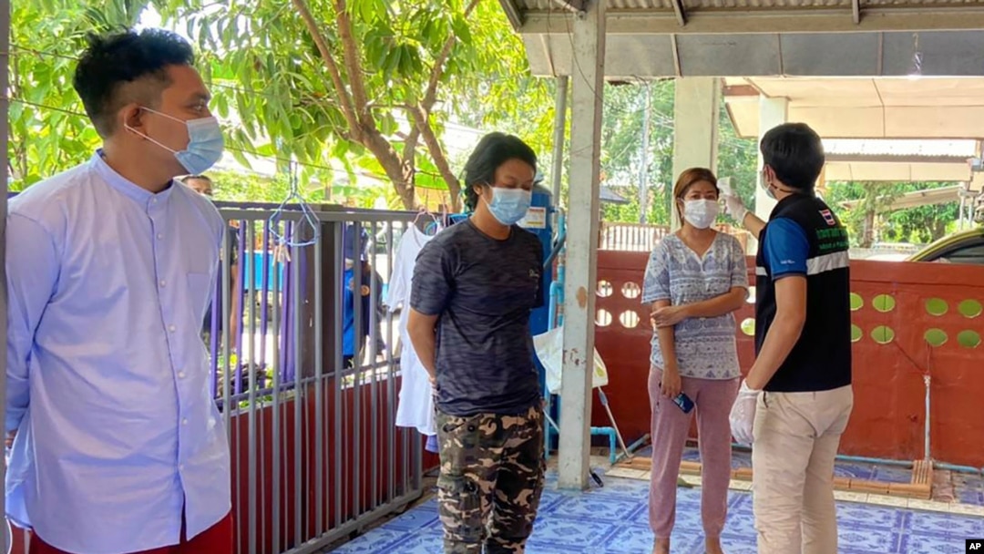 In this photo released by the San Sai District Administrative Office, a Thai officer checks the temperature of journalists working for Democratic Voice of Burma, at San Sai District in Chiang Mai province north of Thailand, May 9, 2021. 